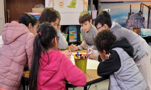 Elementary students gather around a table to complete an activity.